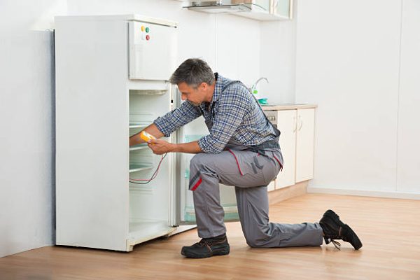 Mature male technician checking fridge with digital multimeter at home